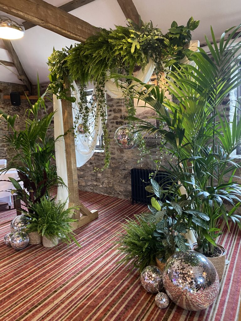 Rustic wooden wedding arch with cascading greenery and palms inside a stone barn venue