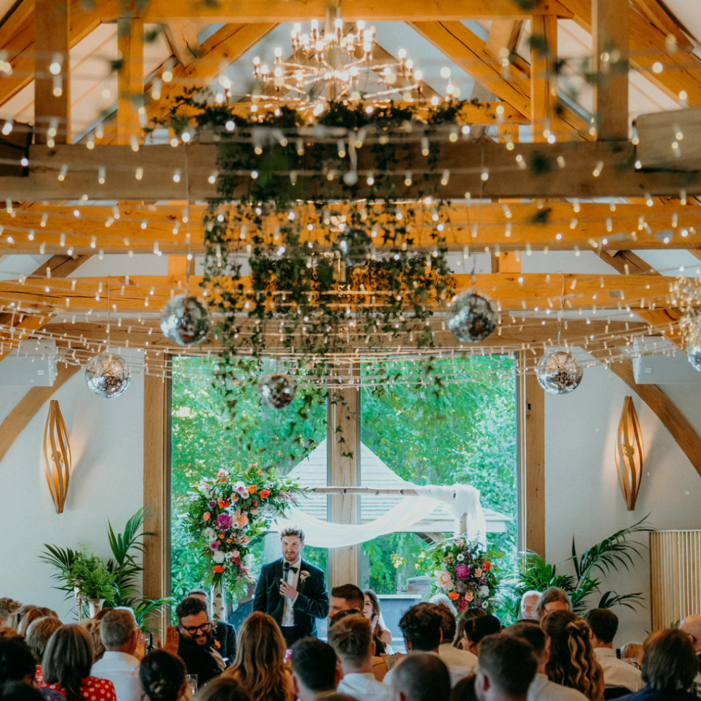 Wedding reception with hanging greenery, fairy lights and disco balls above a ceremony arch with colourful flowers.