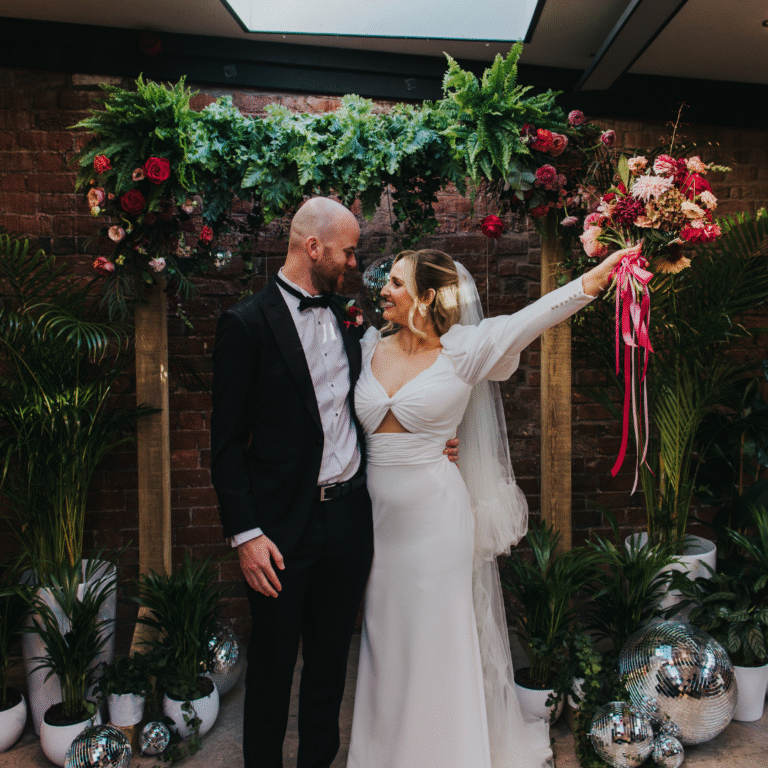 Couple celebrating under greenery wedding canopy with floral arrangements