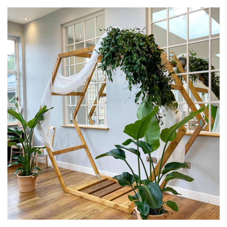 Hexagon wooden wedding arch with white draping and cascading greenery in a bright indoor venue
