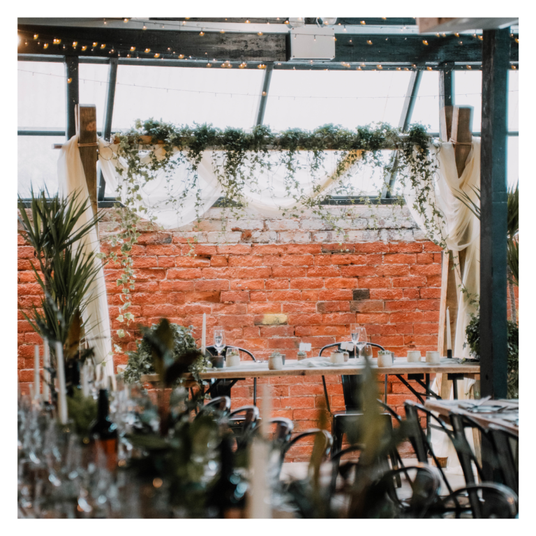Wedding head table backdrop with white draping, trailing greenery and exposed brick wall