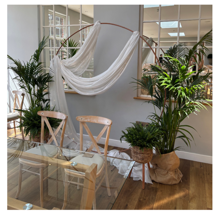 Rose Gold / Copper arch with soft white draping and lush greenery styled behind a wedding signing table.