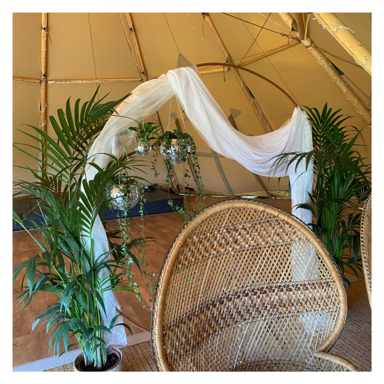 Boho tipi wedding ceremony with rose gold circle backdrop with flowing white drapes, hanging disco balls and lush greenery
