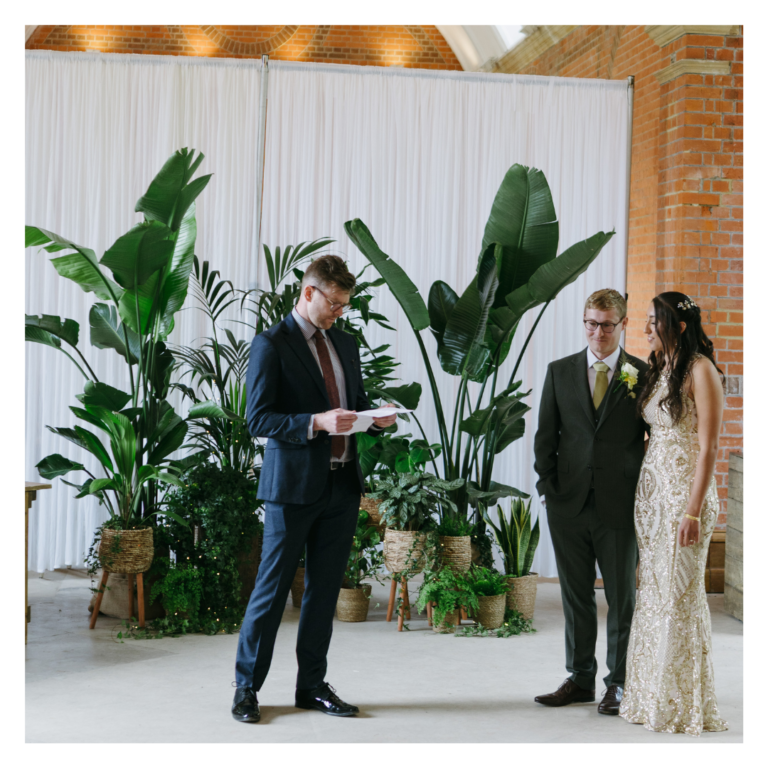 Wedding ceremony with bride and groom standing in front of a lush greenery backdrop.