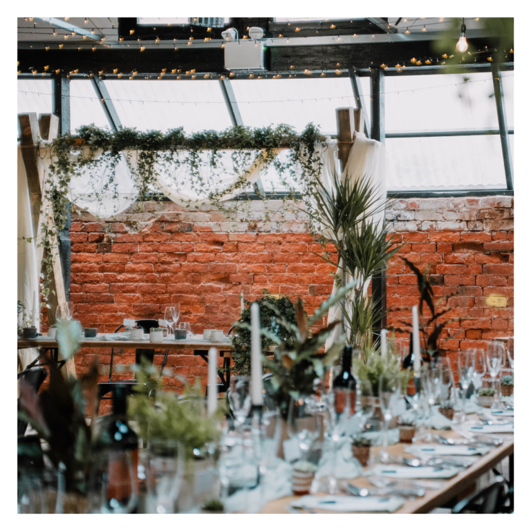 Wedding head table with draped fabric, trailing greenery and exposed brick backdrop