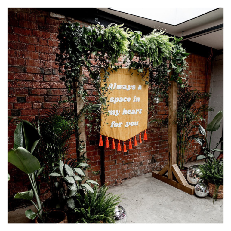 Greenery wedding backdrop with fabric quote banner and disco balls against brick wall