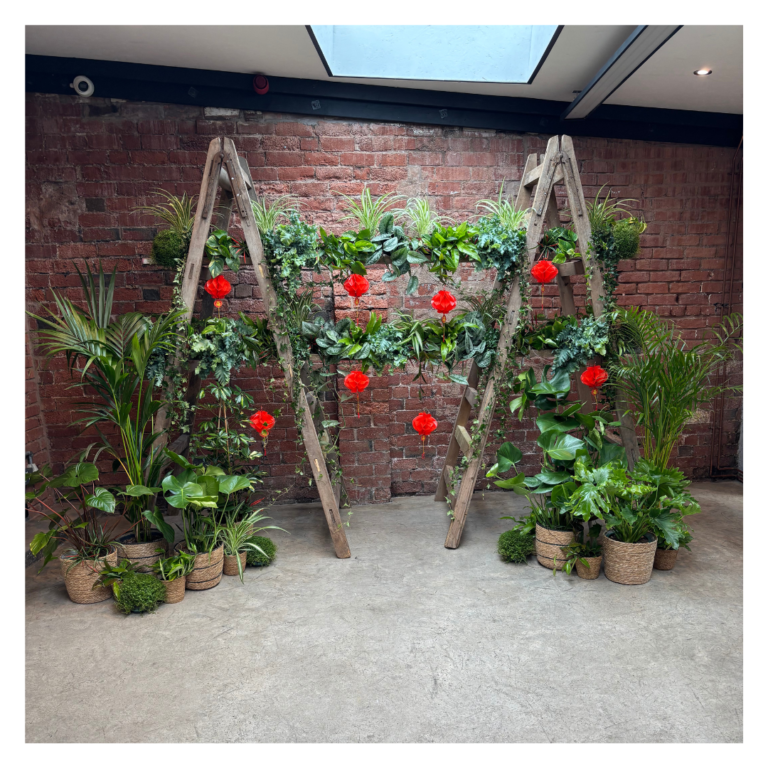 Greenery ladder wedding backdrop with red lanterns and potted plants against a brick wall
