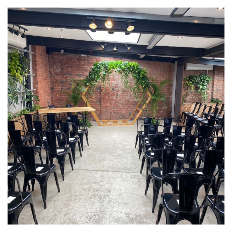 Wedding ceremony seating facing a hexagon greenery arch against an exposed brick wall
