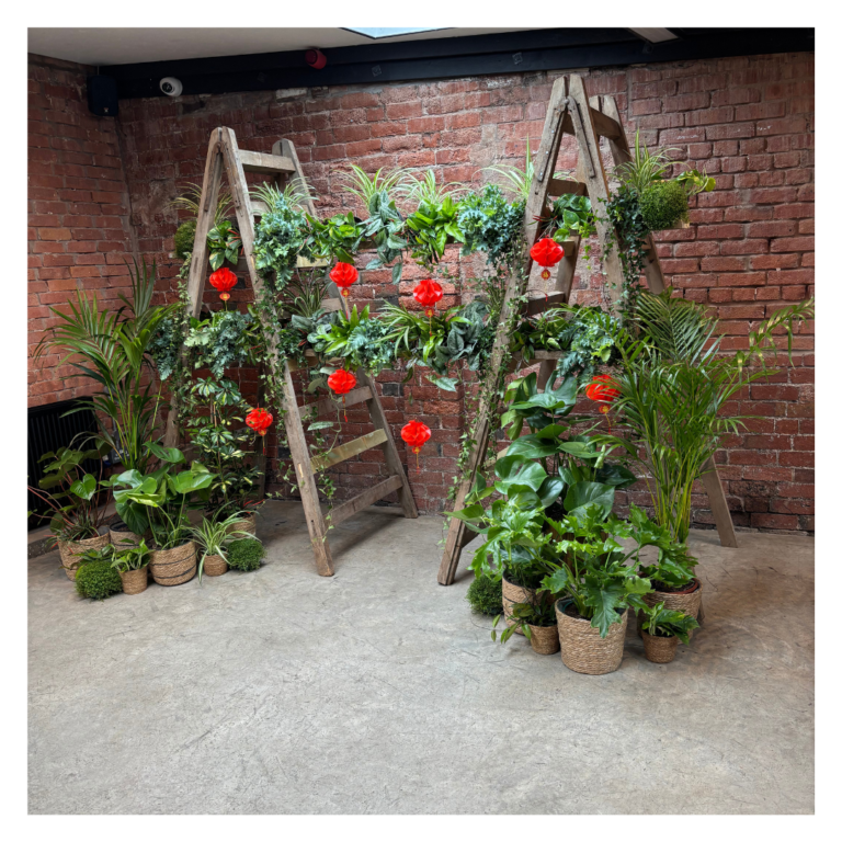 Angled view of a greenery ladder wedding backdrop with red lanterns and lush potted plants