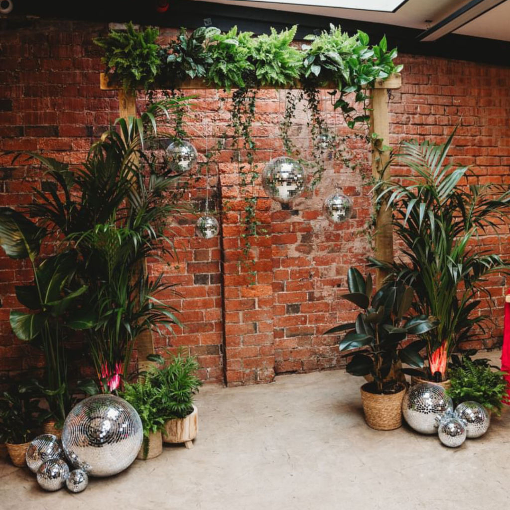 Living plant ceremony backdrop with disco balls against exposed brick at The Shack Revolution industrial wedding venue in Herefordshire.