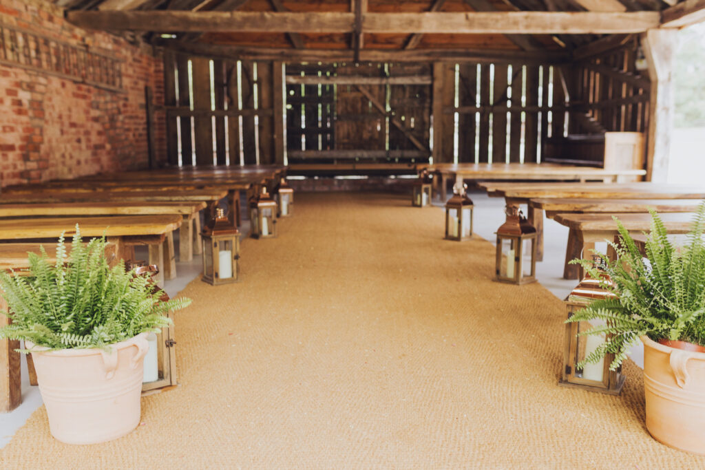 Rustic barn ceremony setup with plant lined aisle and warm wooden interior.