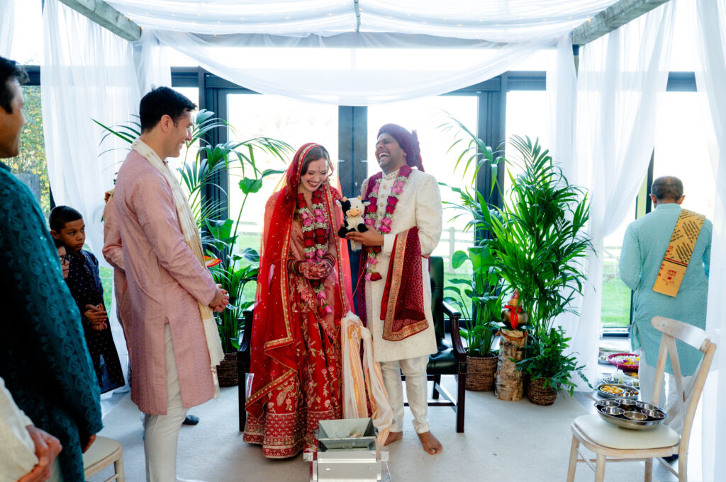 Joyful couple celebrating beneath an eco-friendly mandap at a Crumplebury wedding in Worcestershire, surrounded by lush green plants, soft white draping, and sustainable ceremony décor.